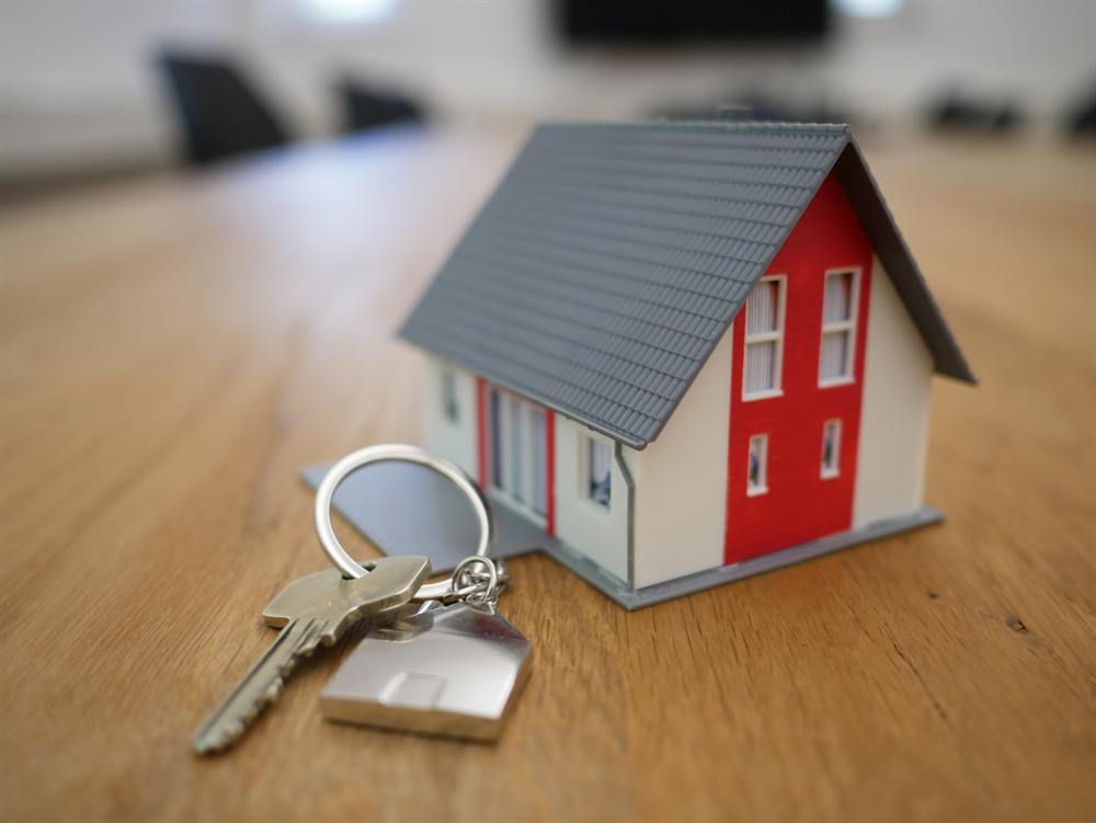 A set of house keys on a table beside a model house.